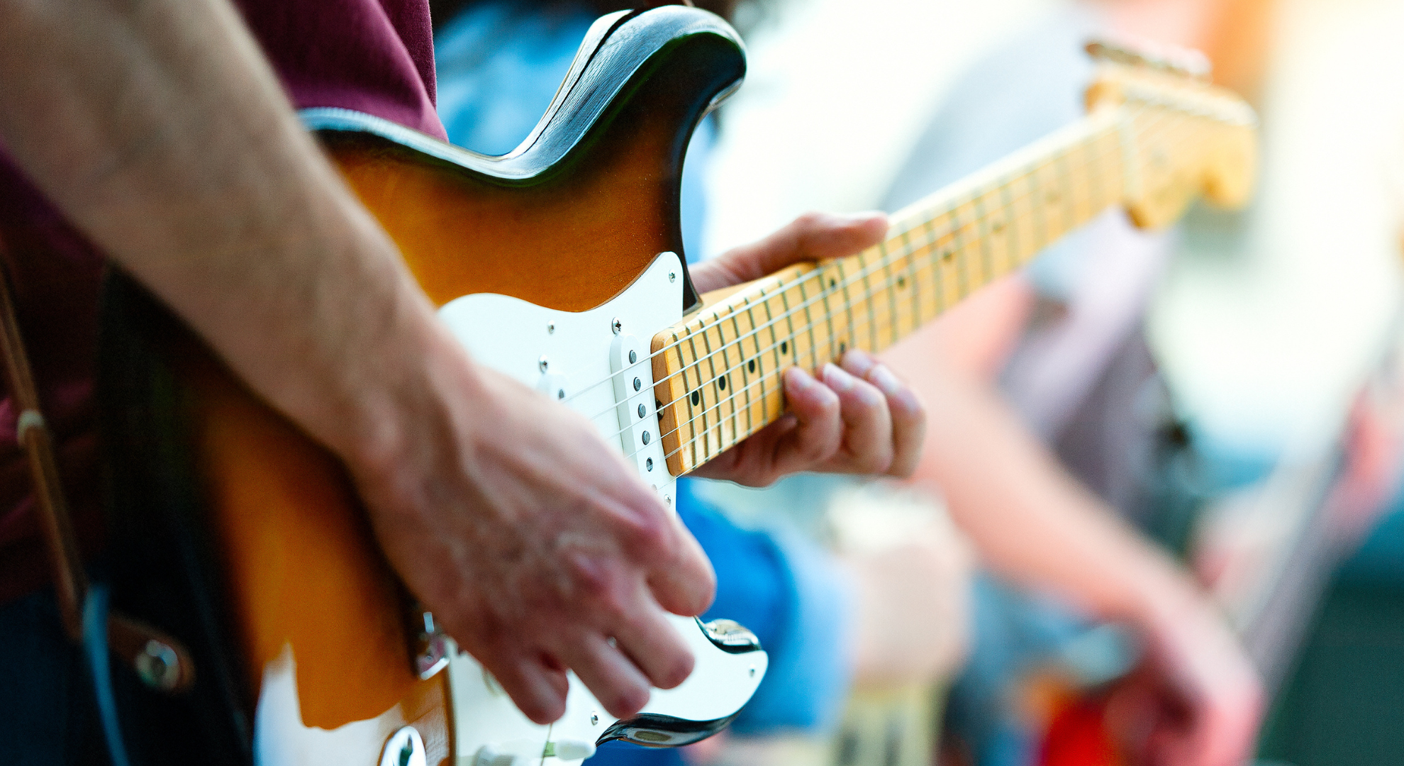 Primo piano delle mani di un chitarrista che suona una chitarra acustica, mostrando le dita che premono le corde e il movimento preciso durante l'esecuzione.